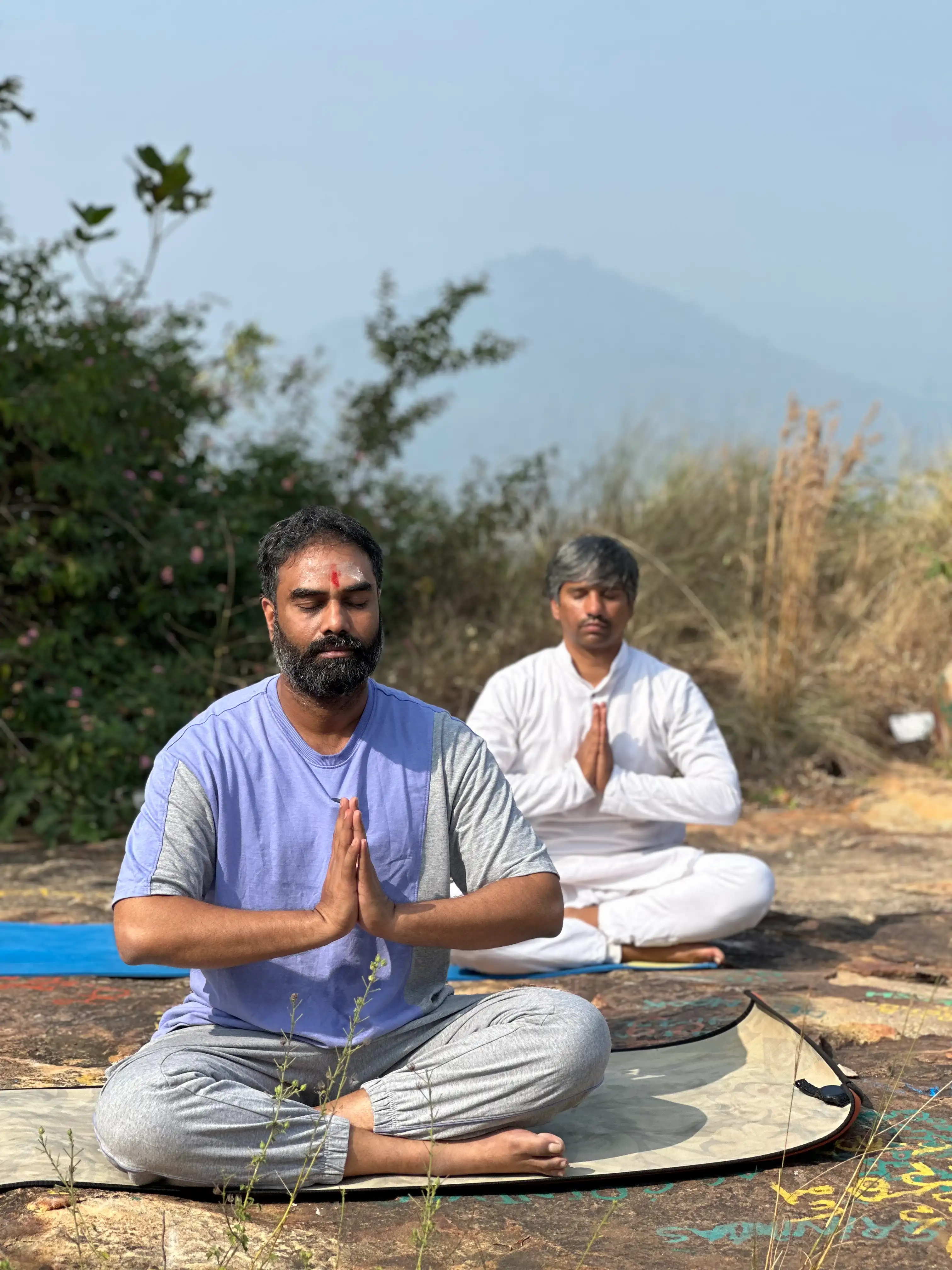 Naveen K. Kolli meditating outdoors on a hilltop with a student